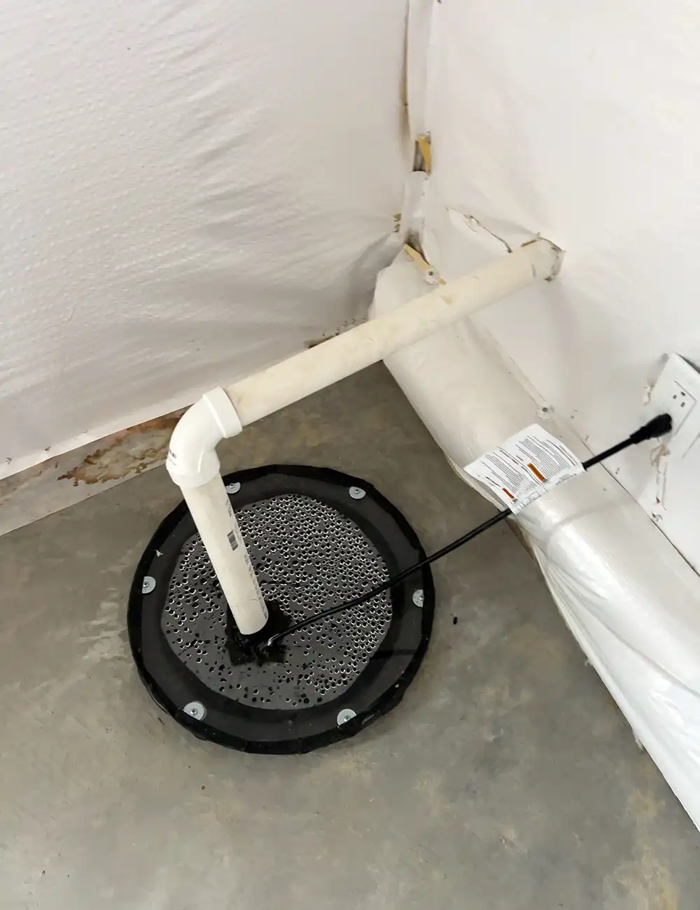 Well pump system with a blue pressure tank, pipes, and gauges, lit by a spotlight on dark ground.