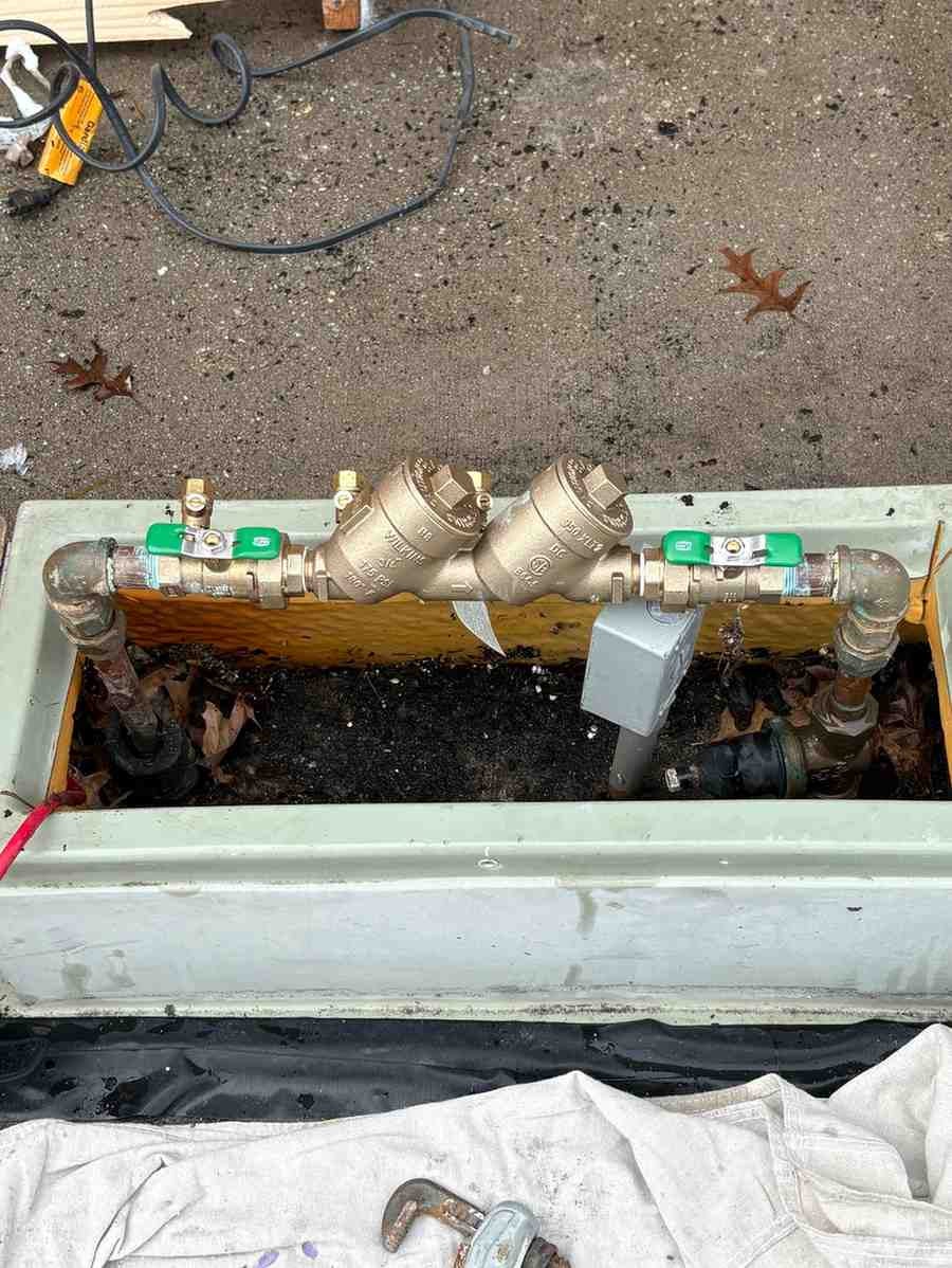 Backflow prevention assembly with two brass valves and green handles, installed in a rectangular outdoor box.